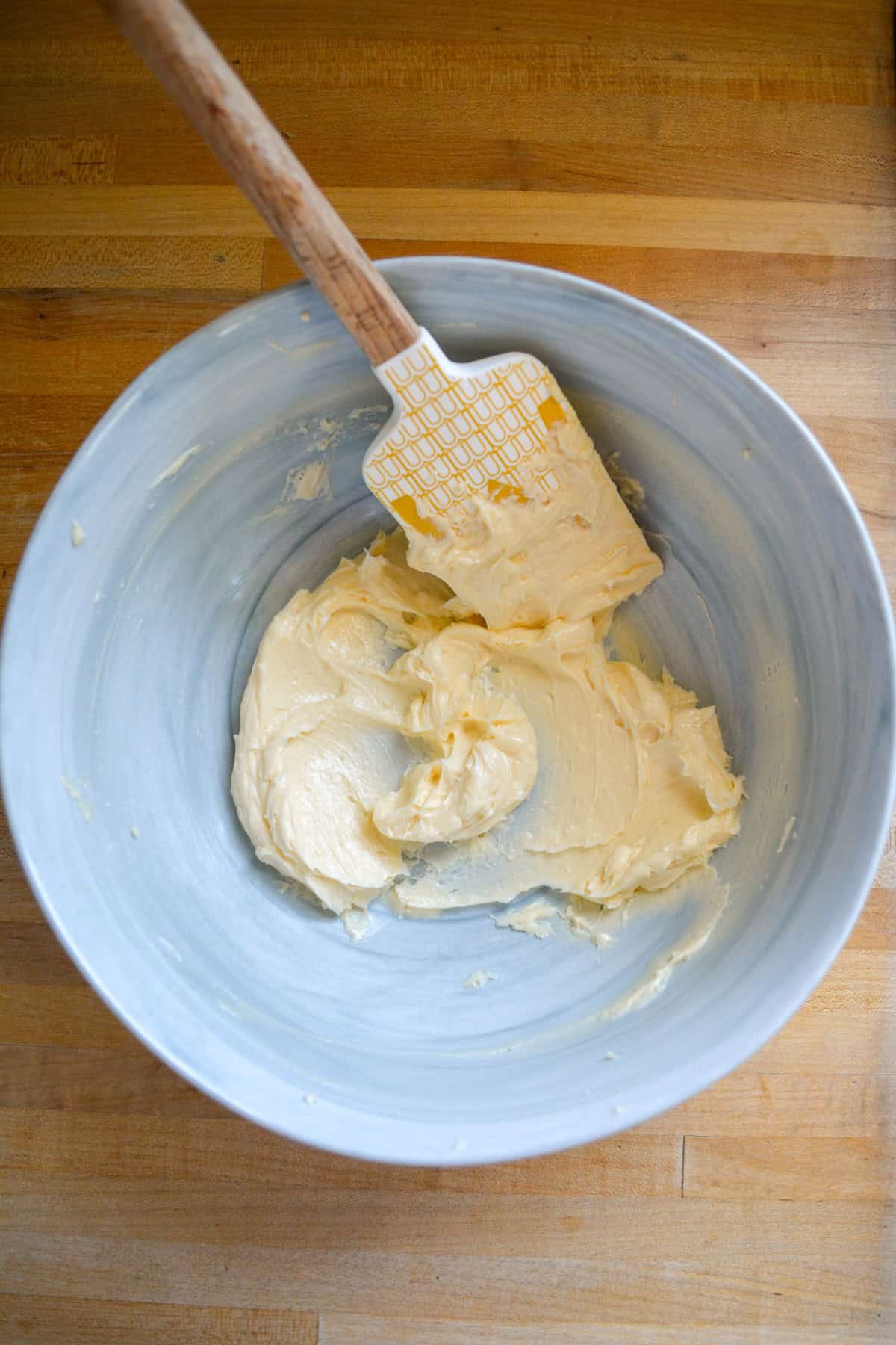 Creamed vegan butter in a large mixing bowl with a rubber spatula inside the bowl.