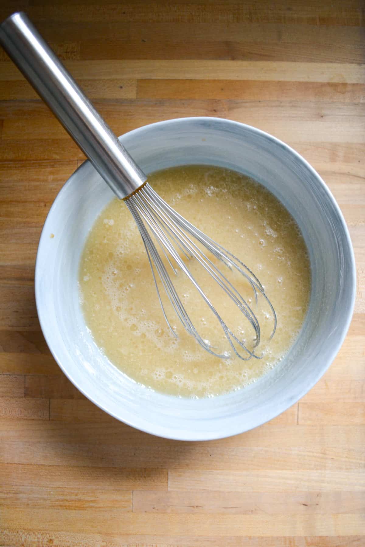 Wet ingredients in a mixing bowl with a metal whisk in the bowl.