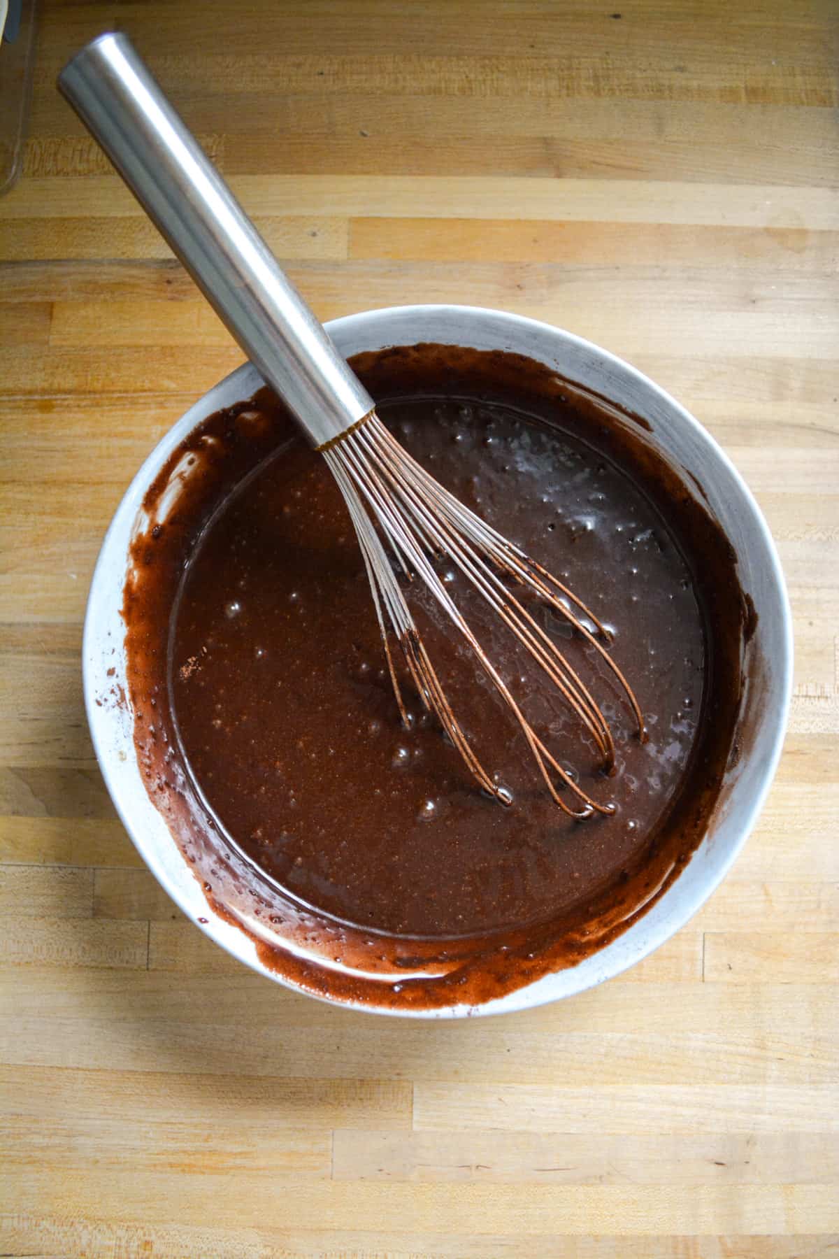 Vegan Gluten Free Chocolate Cake batter mixed together in a mixing bowl. There is a metal whisk in the bowl.