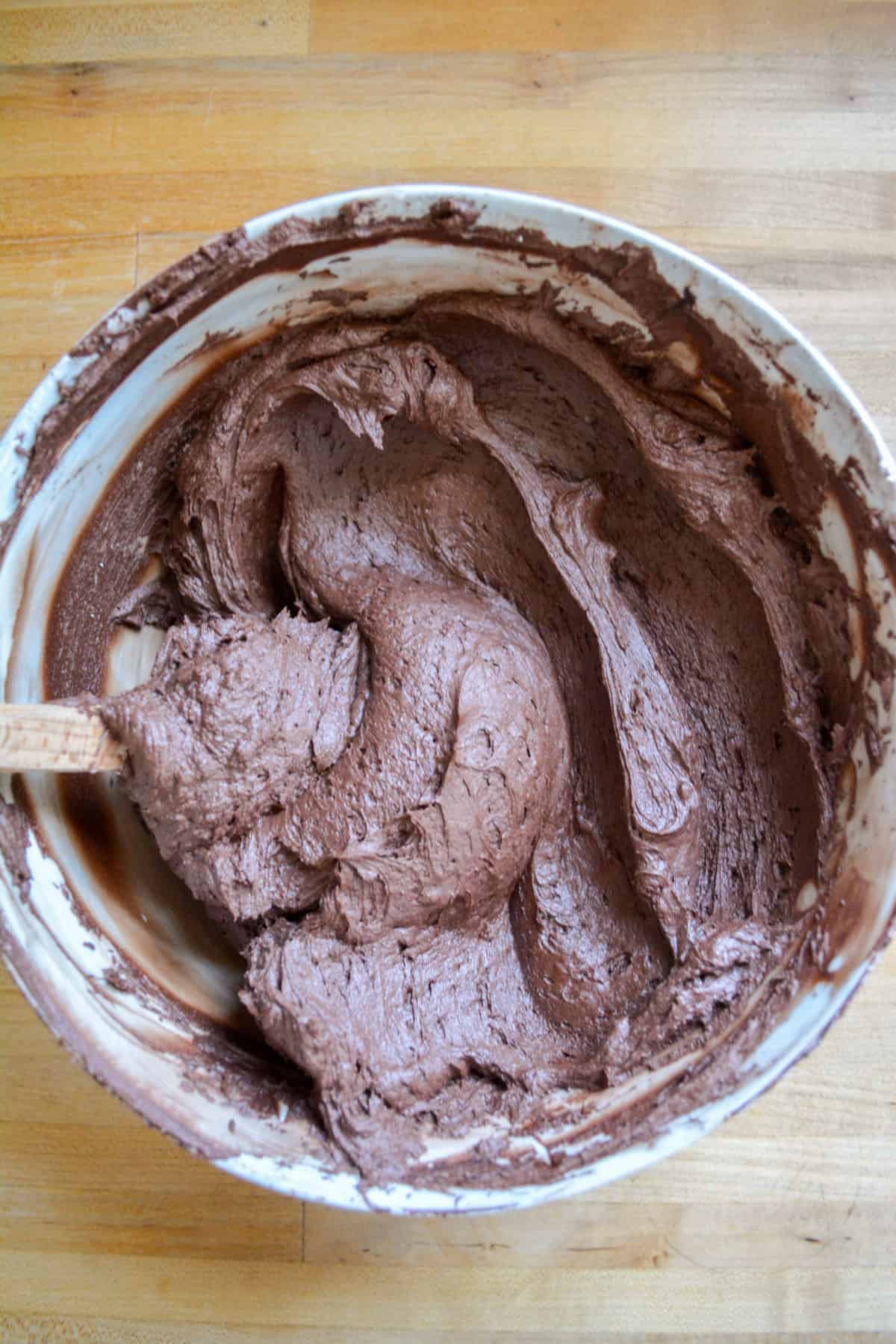 Vegan chocolate buttercream frosting in a mixing bowl with a rubber spatula in the bowl.