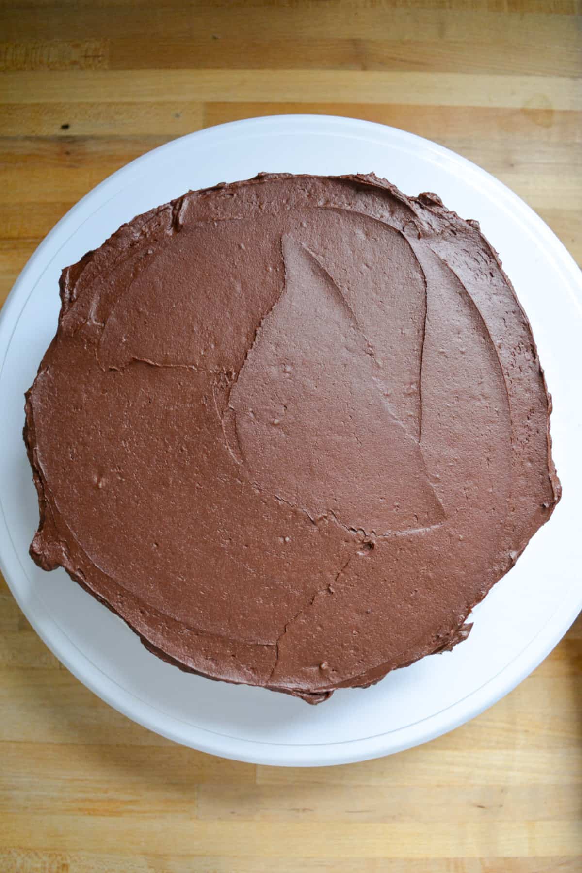 Vegan gluten-free chocolate cake frosting with chocolate frosting on a cake board.