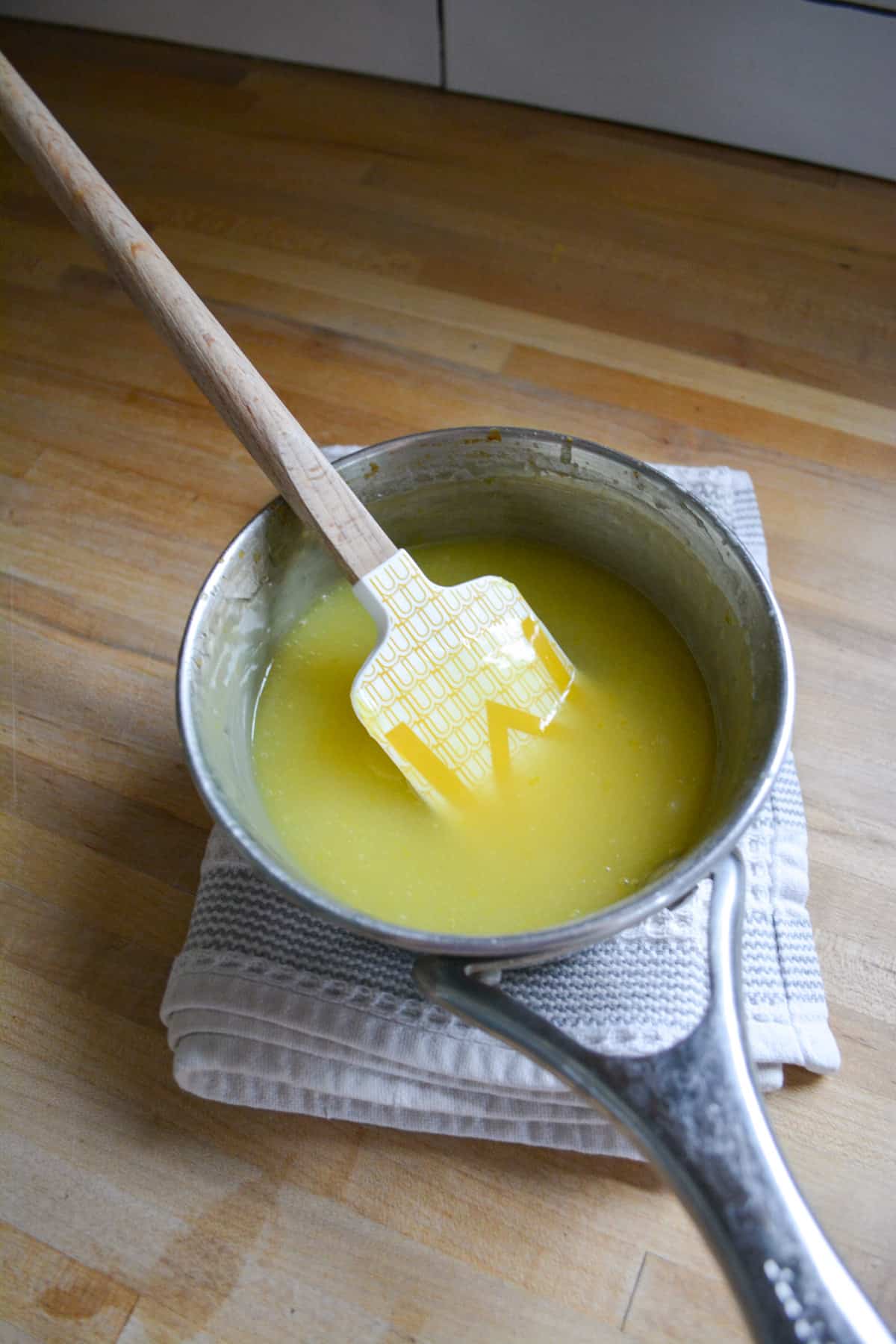 Finished lemon curd in a small metal sauce pan with a rubber spatula in it.