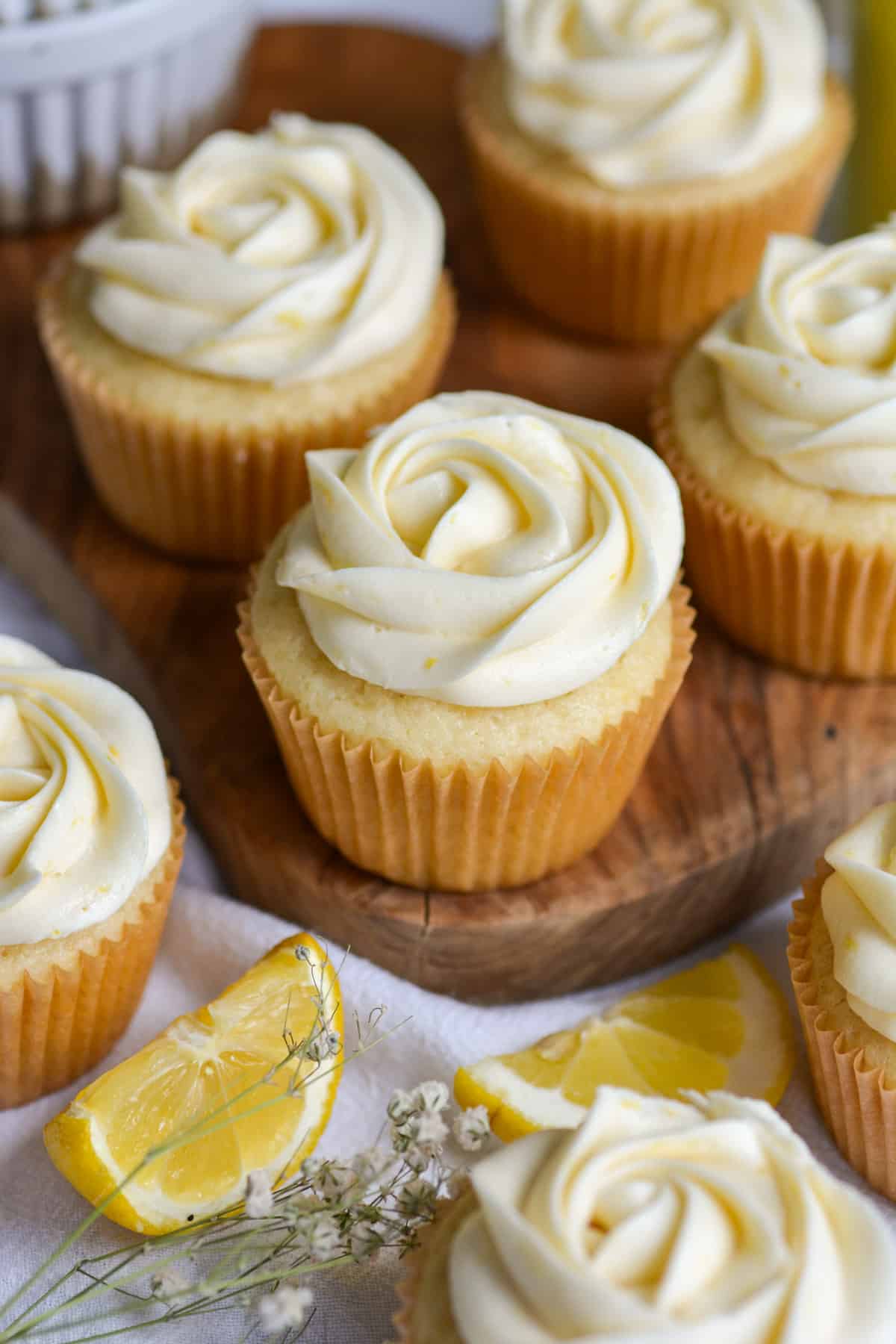Vegan Lemon Curd Filled Cupcakes on a small wooden board with lemon slices in the foreground.