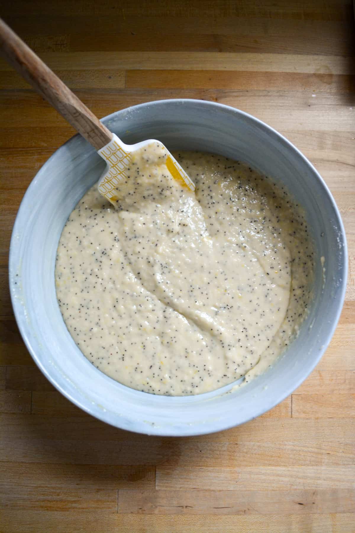 Mixed Vegan Lemon Poppy Seed Muffin batter in a mixing bowl with a rubber spatula in it.