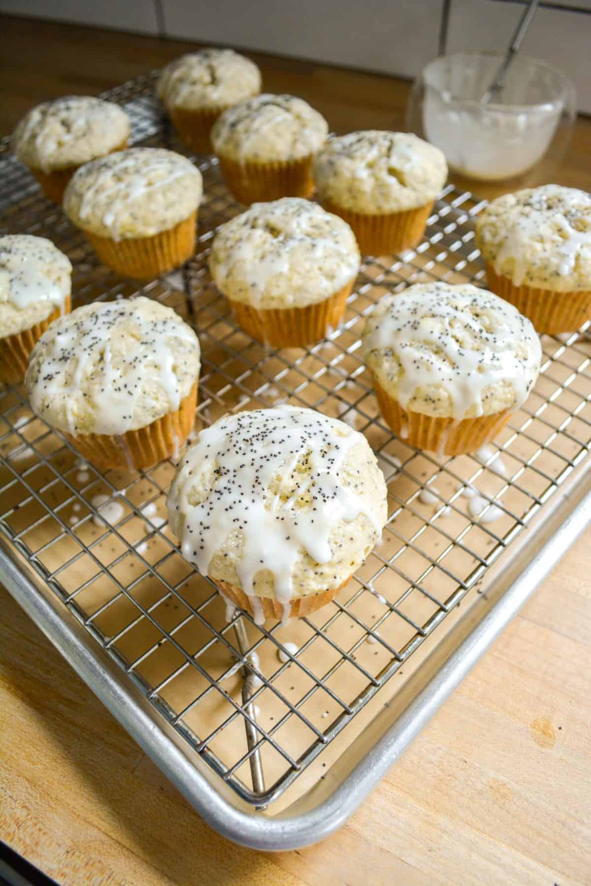 Glazed Vegan Lemon Poppy Seed Muffins on a wire cooling rack that is over a baking sheet.
