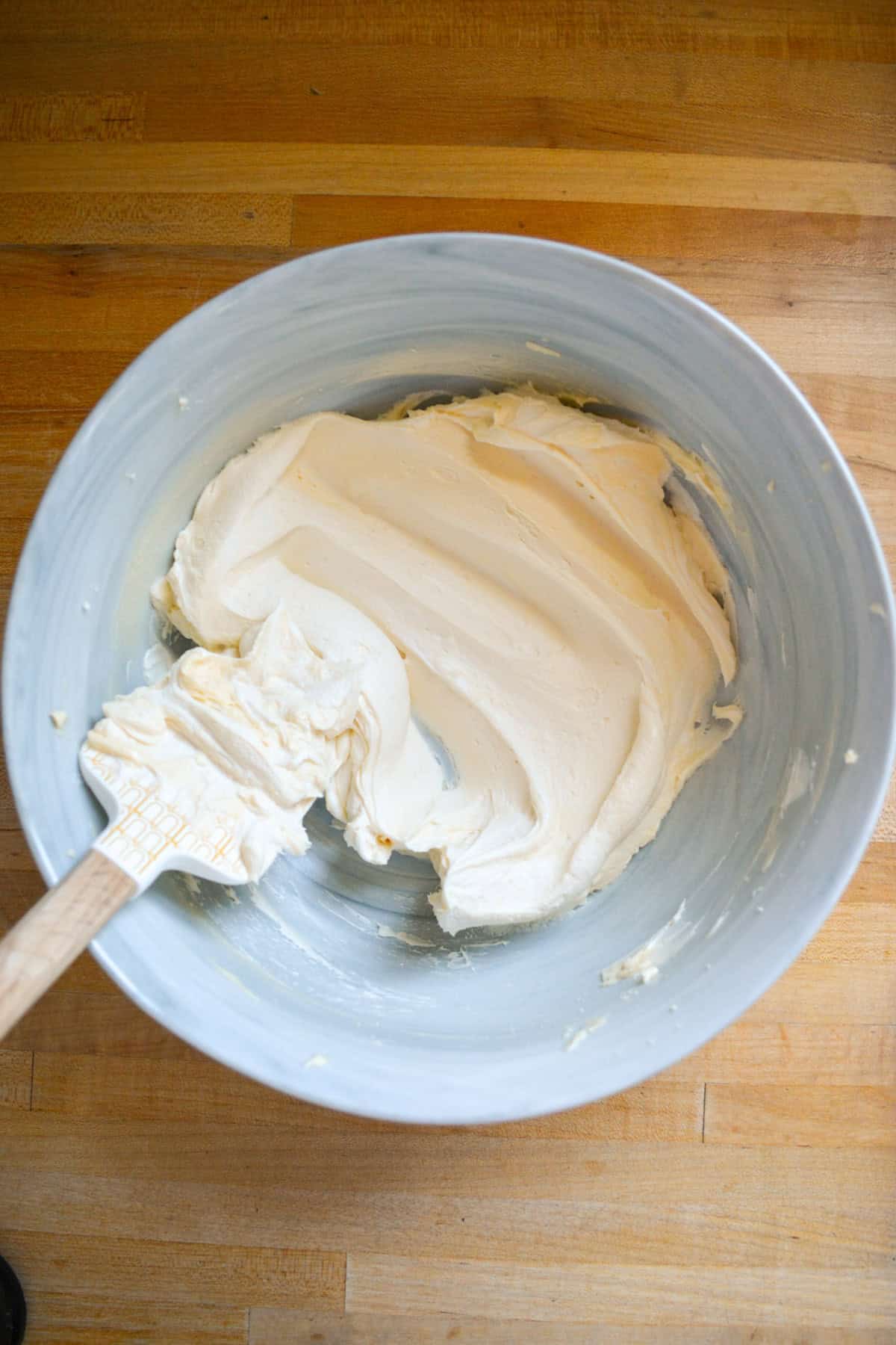 Vegan butter and cream cheese creamed together in a mixing bowl with a rubber spatula in the bowl.
