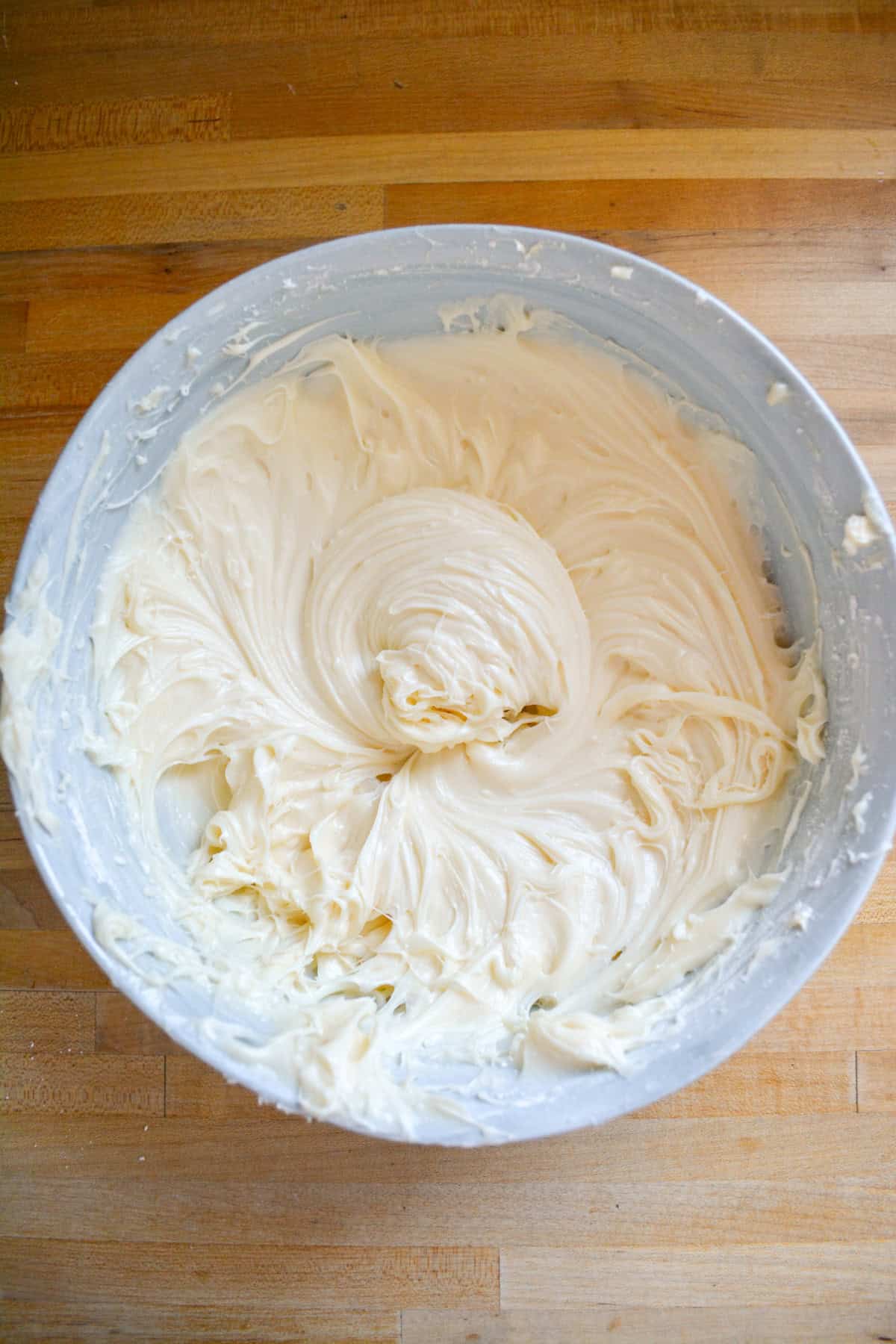 Vegan cream cheese frosting in a mixing bowl on a wooden surface.