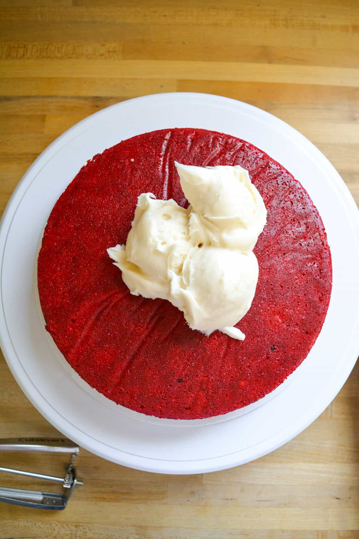 Vegan red velvet cake on a cake board with scoops of vegan cream cheese frosting on top.