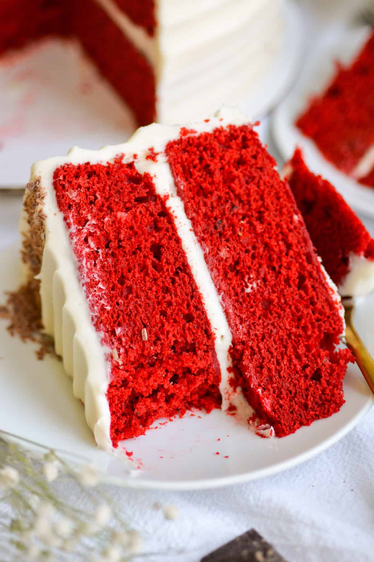 Vegan red velvet cake slice on a plate with a bite taken out of it.