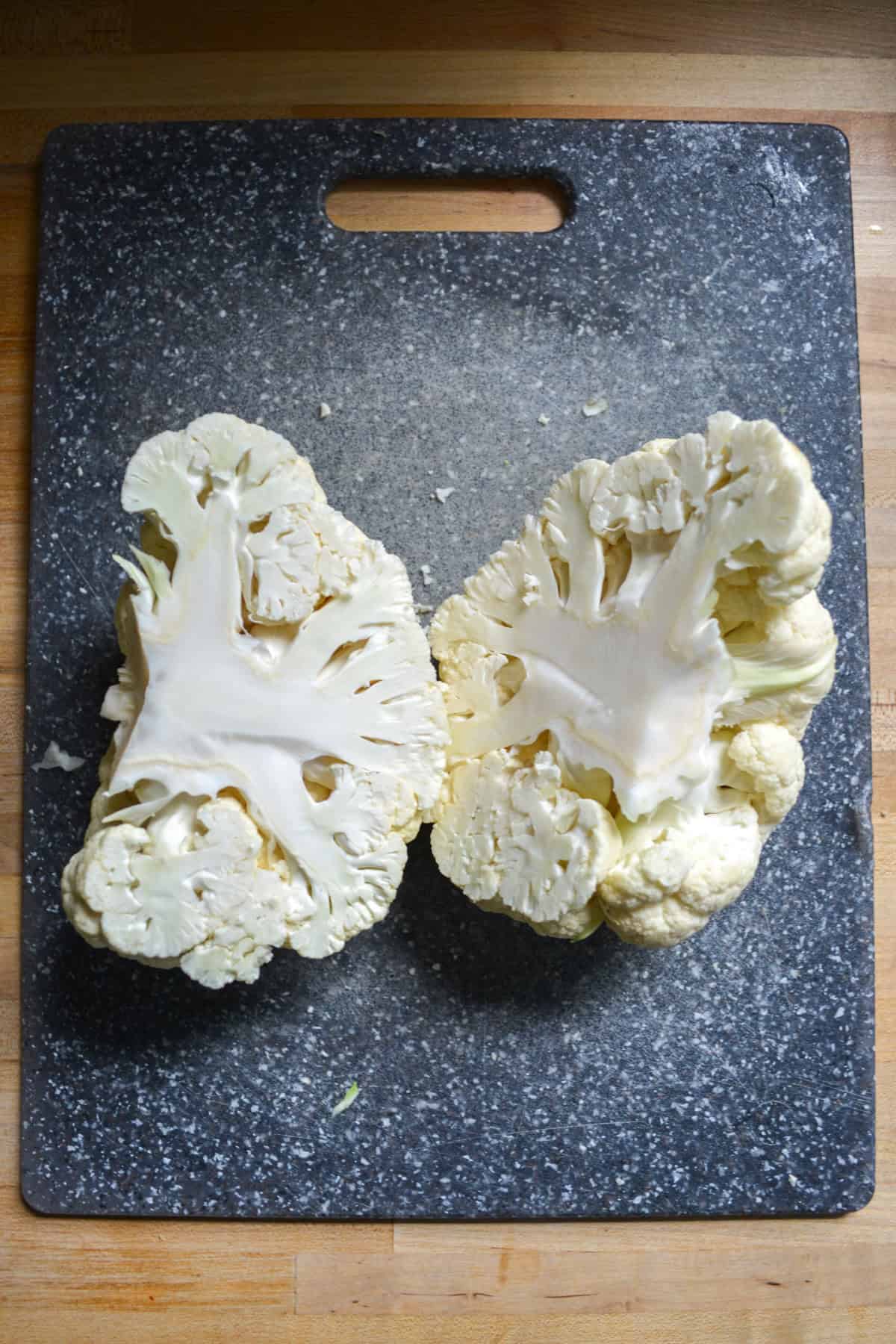 Cauliflower cut in half on a cutting board.