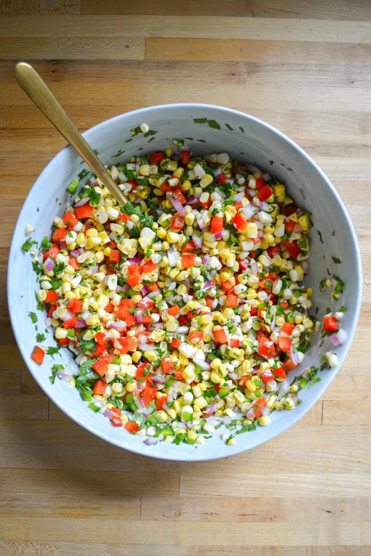 Corn salsa in a large mixing bowl with a spoon in it.