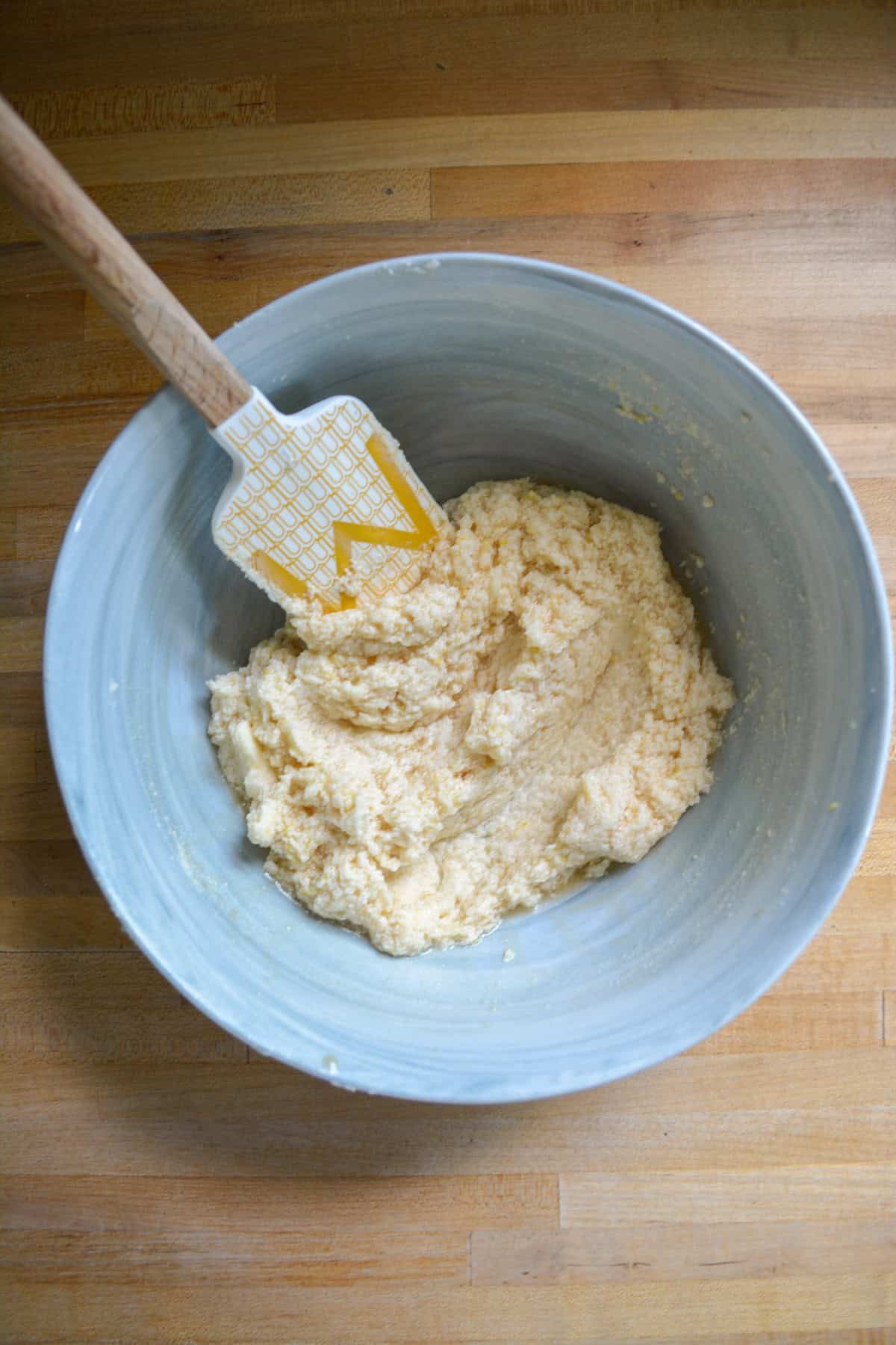 Non-dairy milk and vanilla added into the creamed butter and sugar mixture in a large mixing bowl with a rubber spatula to the top left of the bowl.