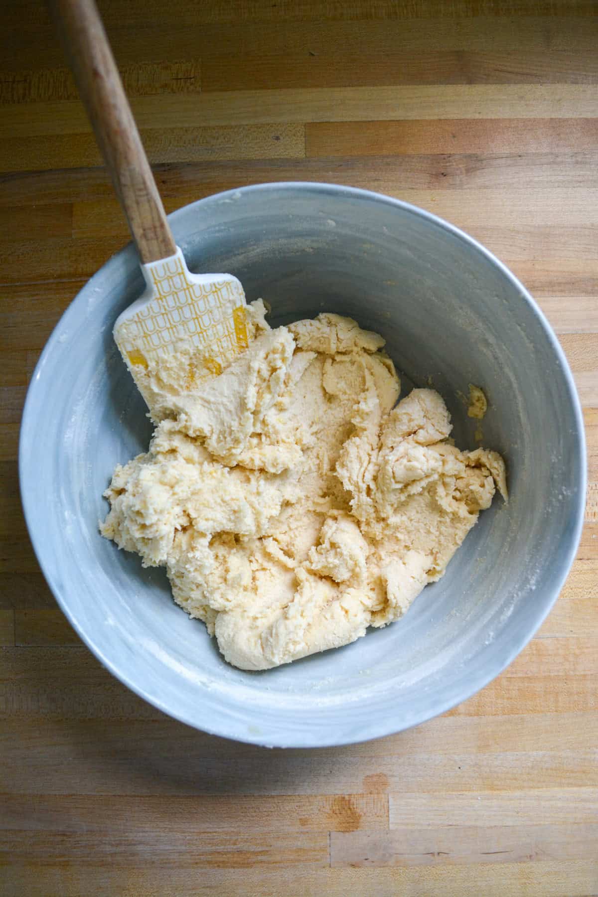 The dry mixture mixed in to form a cookie dough in a large mixing bowl with a wooden spoon to the top left.