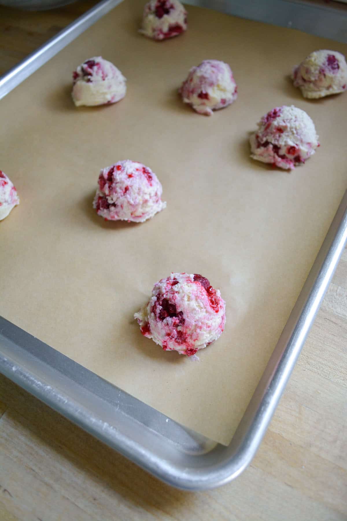 Raspberry cookies scooped onto a parchment-lined sheet trat.