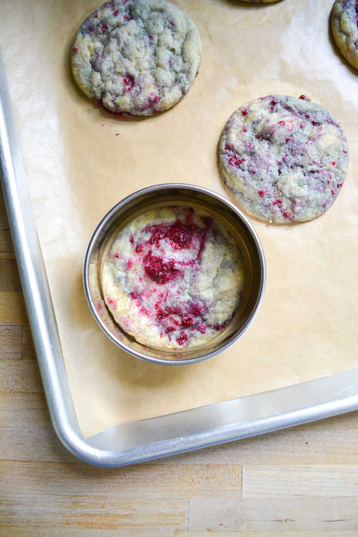 A large round cookie cutter around a baked raspberry cookie to reshape it.