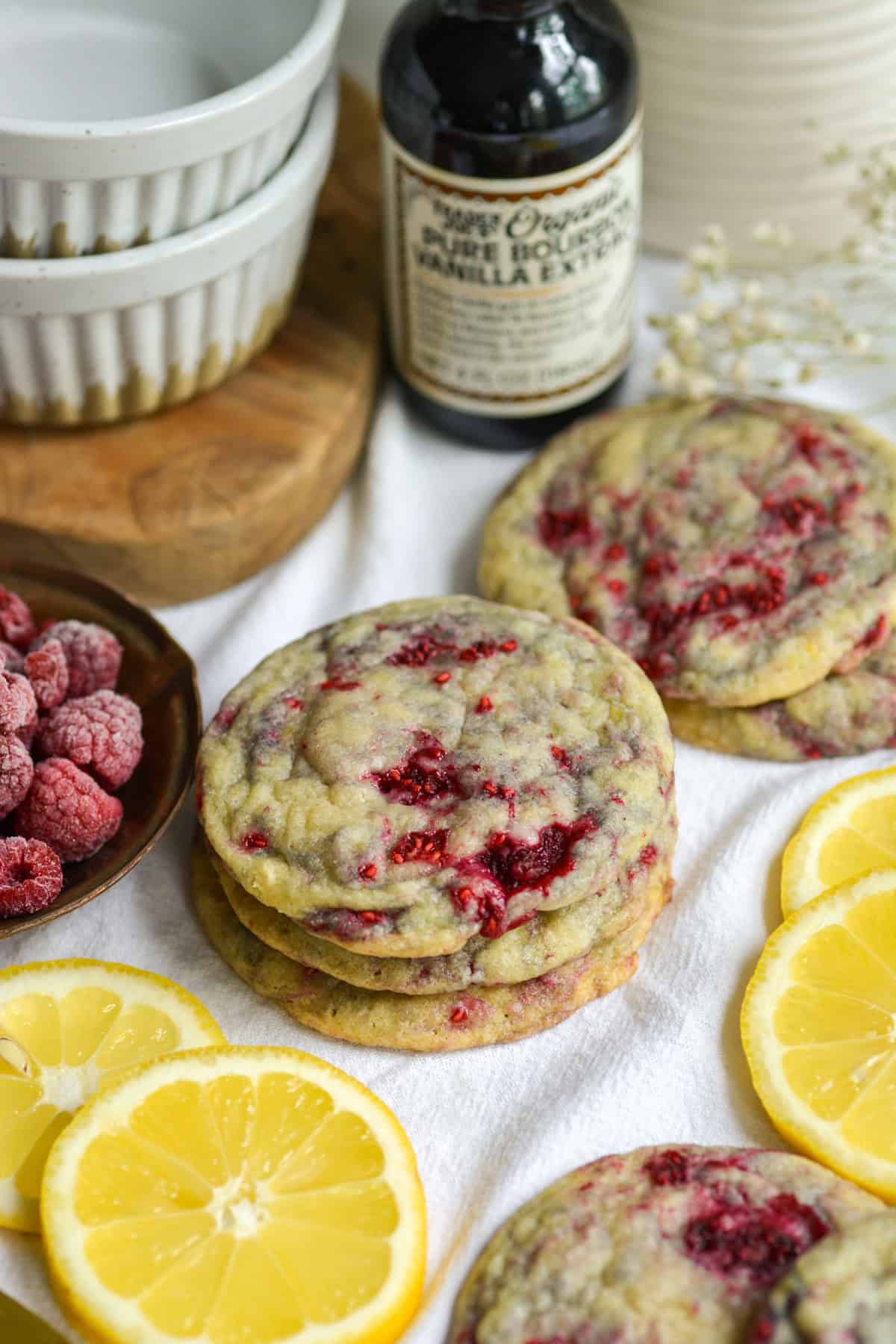 3 Vegan Lemon Raspberry Cookies stacked on top of each other on a white cloth with slices of lemon in the scene.