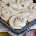Vegan Banana Bread Cinnamon Rolls frosted with cream cheese frosting in a baking pan.