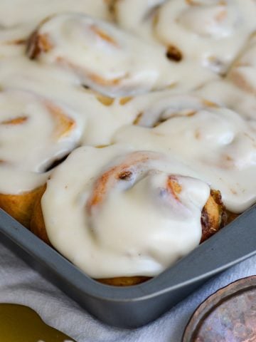 Vegan Banana Bread Cinnamon Rolls frosted with cream cheese frosting in a baking pan.