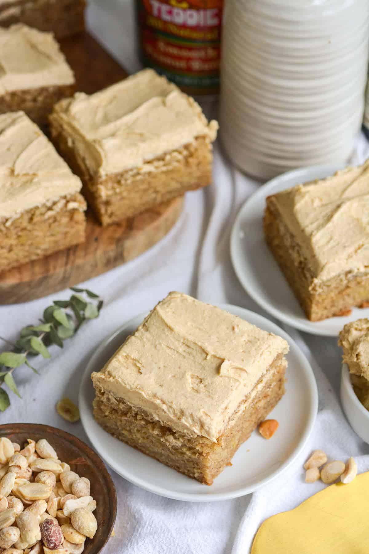 Two slices of Vegan Banana Cake with peanut butter frosting on sall plates and more slices on a small wooden board in the background.