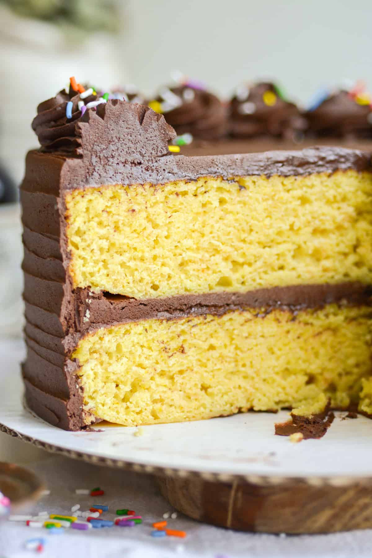 Vegan Birthday cake with slices taken out of it to show the cross-section of the cake. Two layers of yellow cake with chocolate frosting in between and on top.
