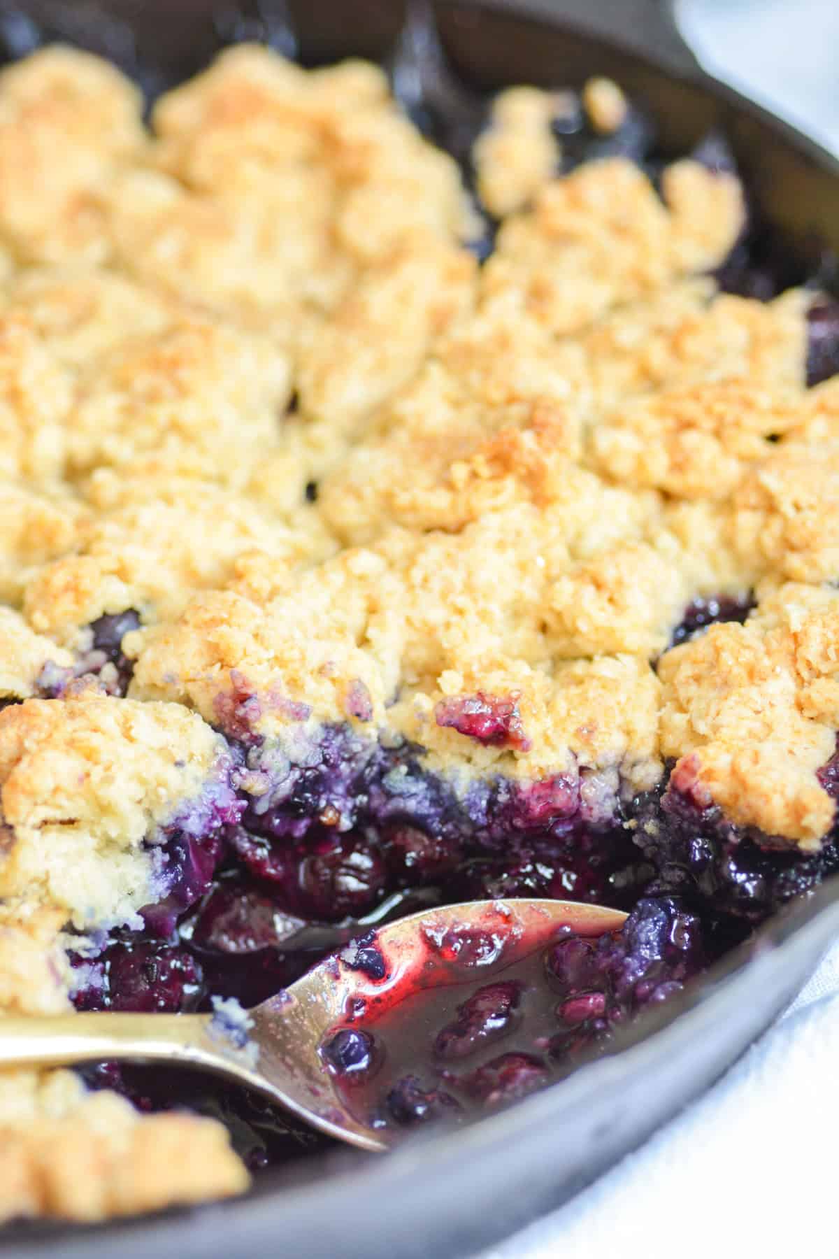 Vegan Blueberry Cobbler in a skillet with a scoop taken out of it.