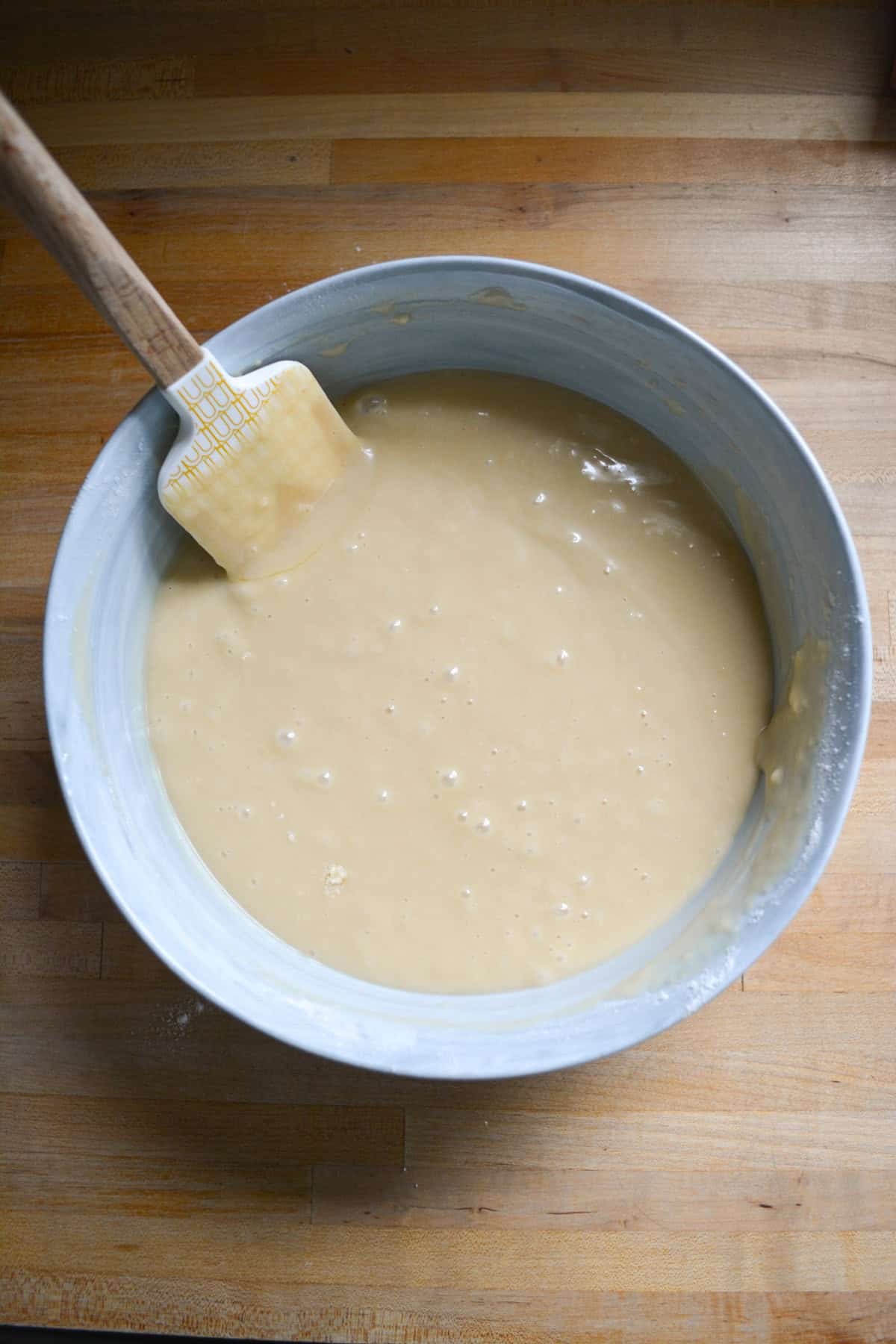 Vegan vanilla cake batter in a mixing bowl with a rubber spatula in the top left corner.