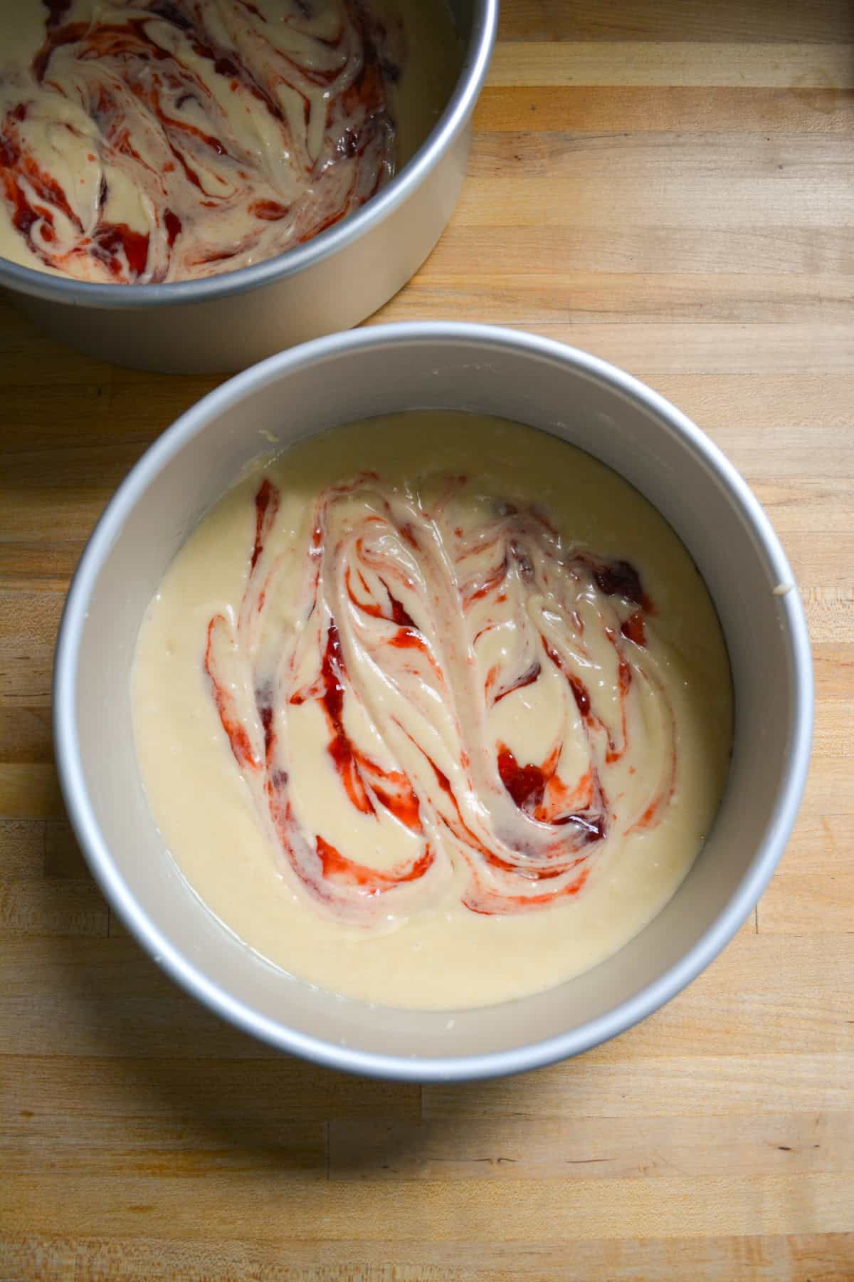 Cake batter portioned into an 8 inch round cake pan with strawberry jam swirled into the batter.