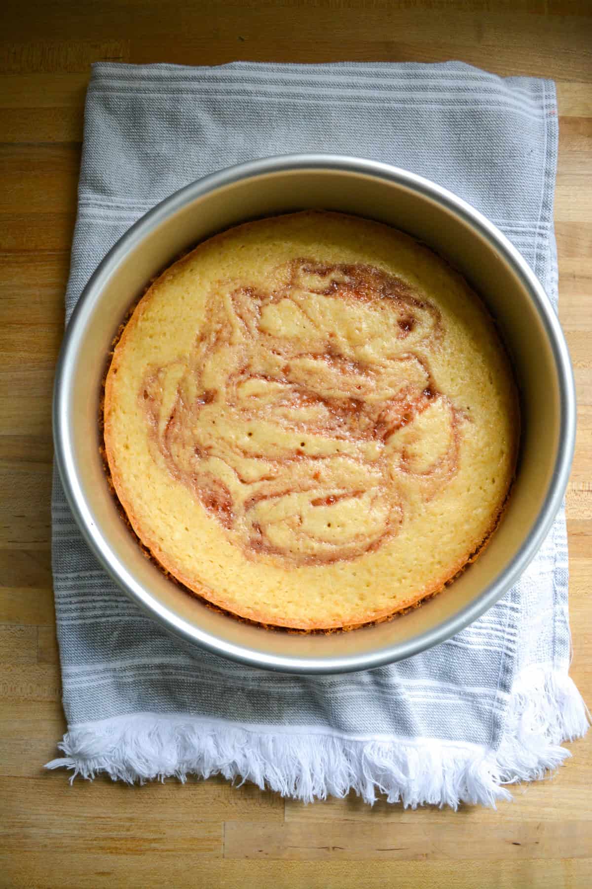 Baked cake in a round cake pan with strawberry preserves swirled into the top.