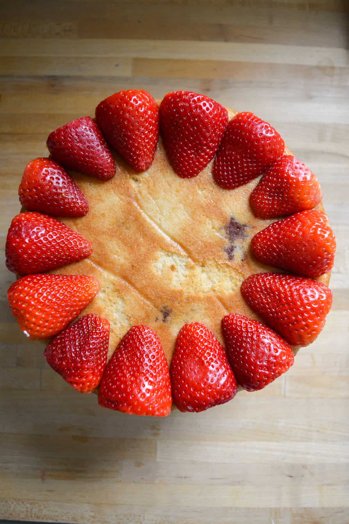 Cake layer upside down on a cake board with halved strawberries lining the perimeter of the cake.