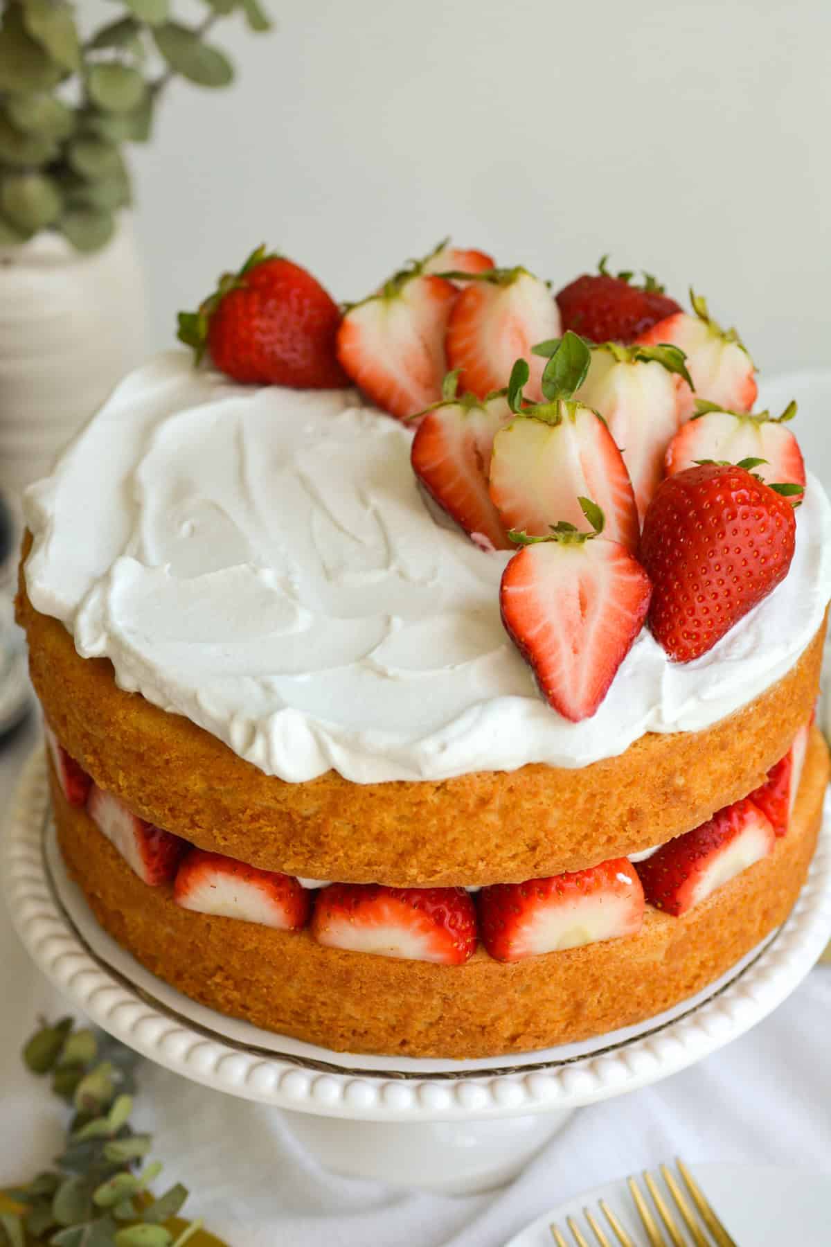 Finished Vegan Strawberry Shortcake Cake on a cake stand, topped with vegan whipped cream and strawberries.