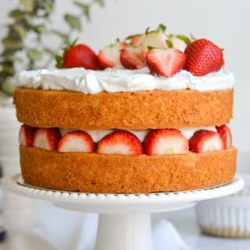Vegan Strawberry Shortcake Cake on a white cake stand. The cake is a two-layer cake with strawberries and whipped cream in between the layers and on top.