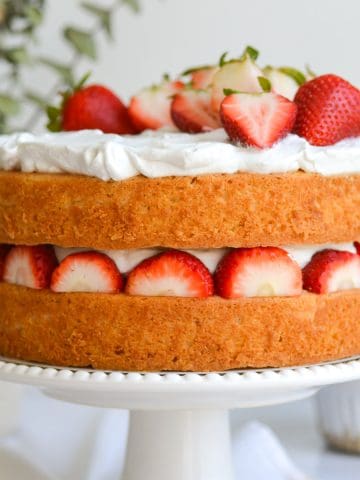 Vegan Strawberry Shortcake Cake on a white cake stand. The cake is a two-layer cake with strawberries and whipped cream in between the layers and on top.