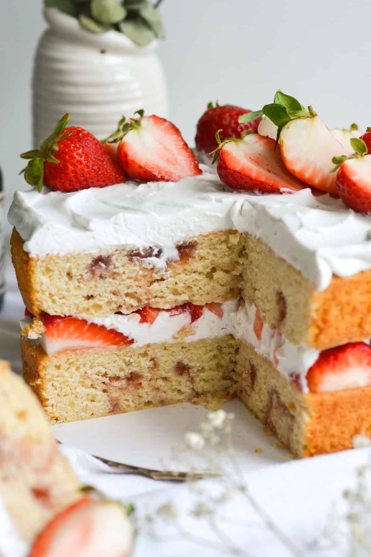 Vegan Strawberry Shortcake Cake with slices taken out of it to show the middle of the cake. Its topped with vegan whipped cream and strawberries.