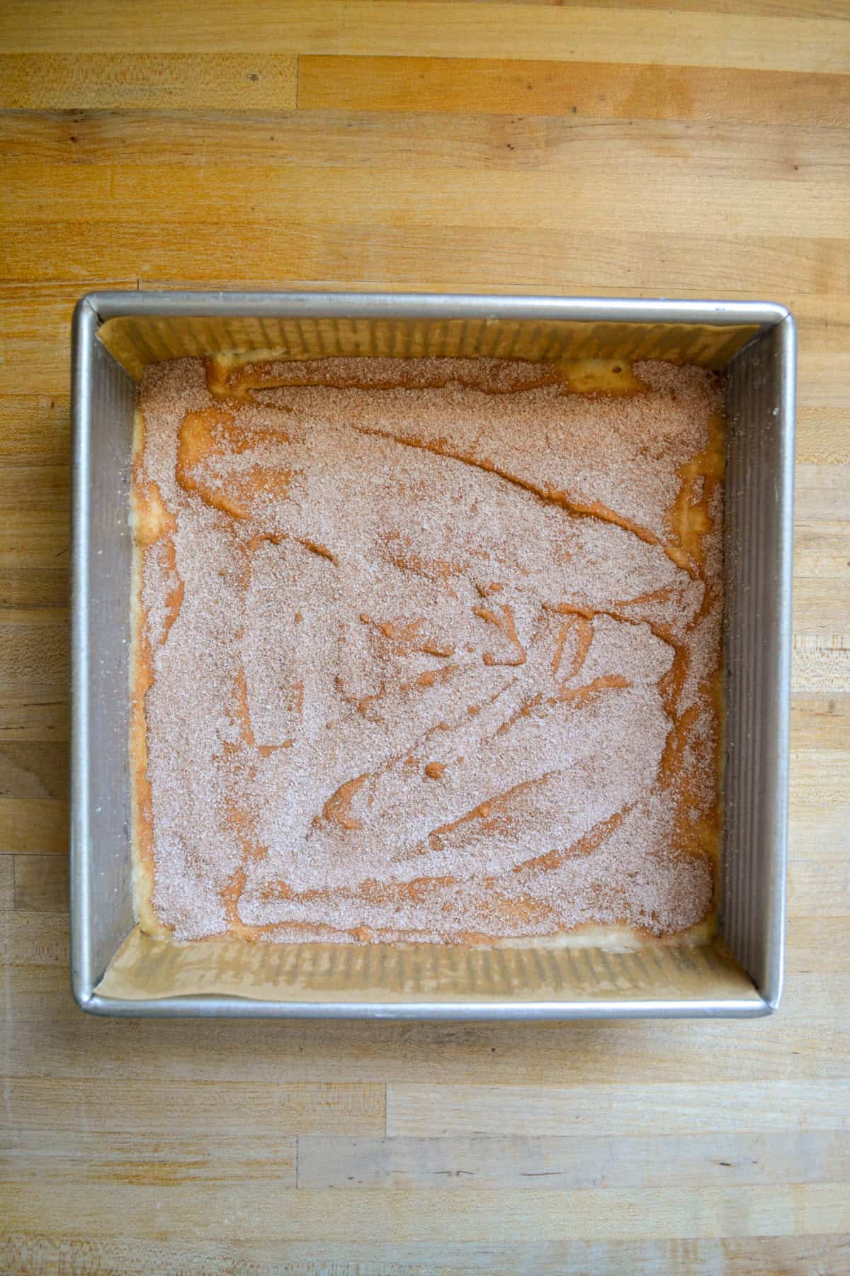 Cake batter topped with cinnamon sugar in a square baking pan.