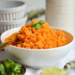 Vegan Gluten Free Mexican Rice in a bowl with a spoon in it with ramekins in the background.