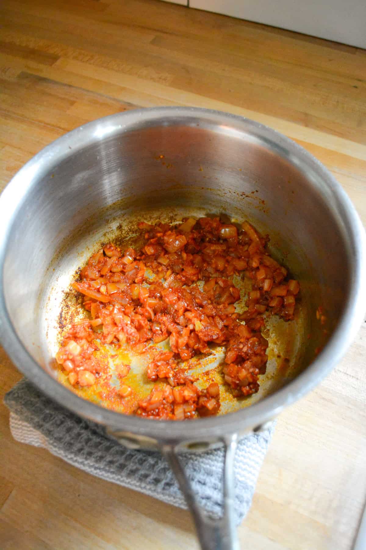 Tomato paste and spices added to the onion in the saucepan.