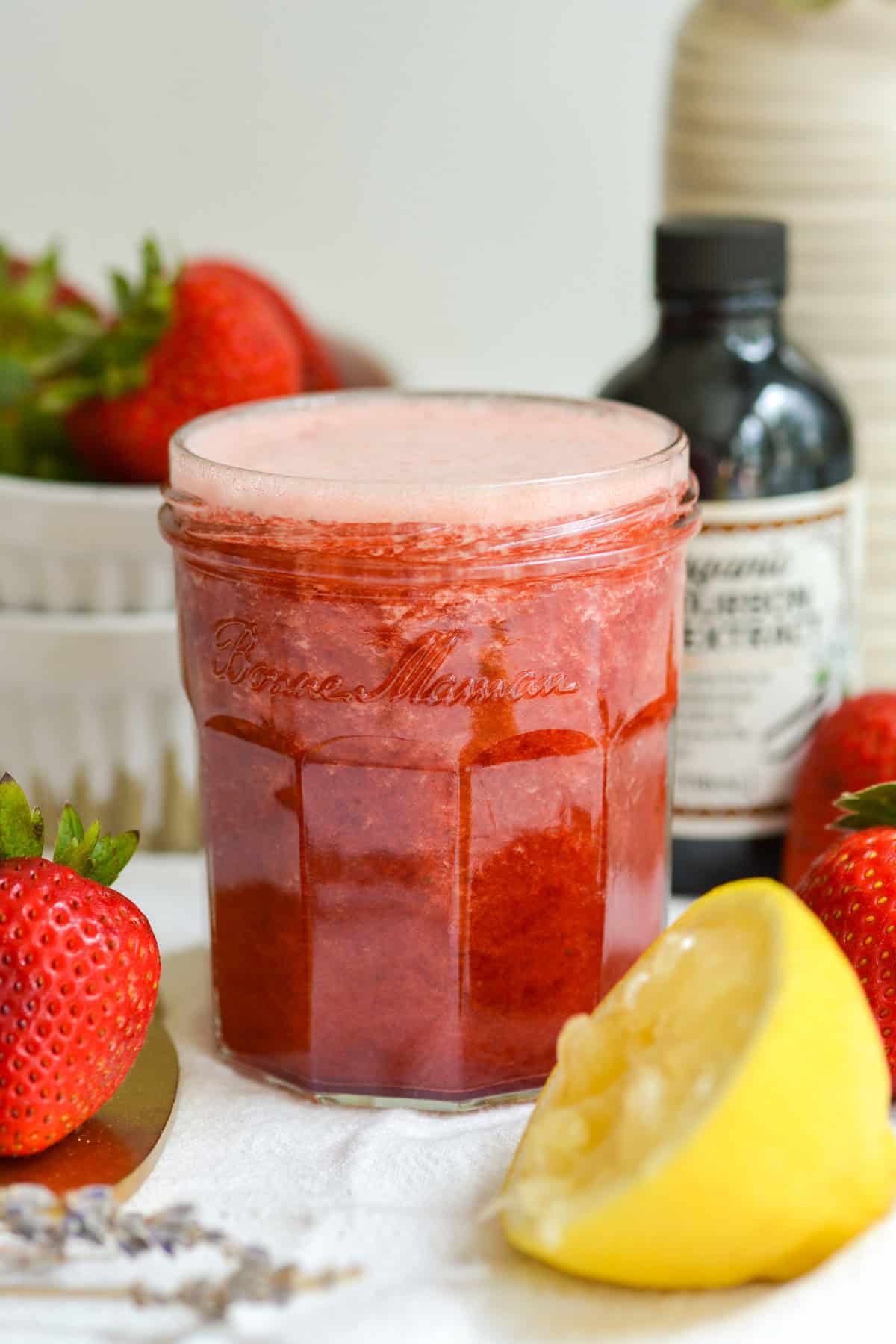 Strawberry Simple Syrup in a jar with a lemon wedge in the foreground.