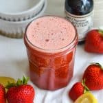 Strawberry Syrup for Drinks and Cocktails in a jar with fresh strawberries in the scene.