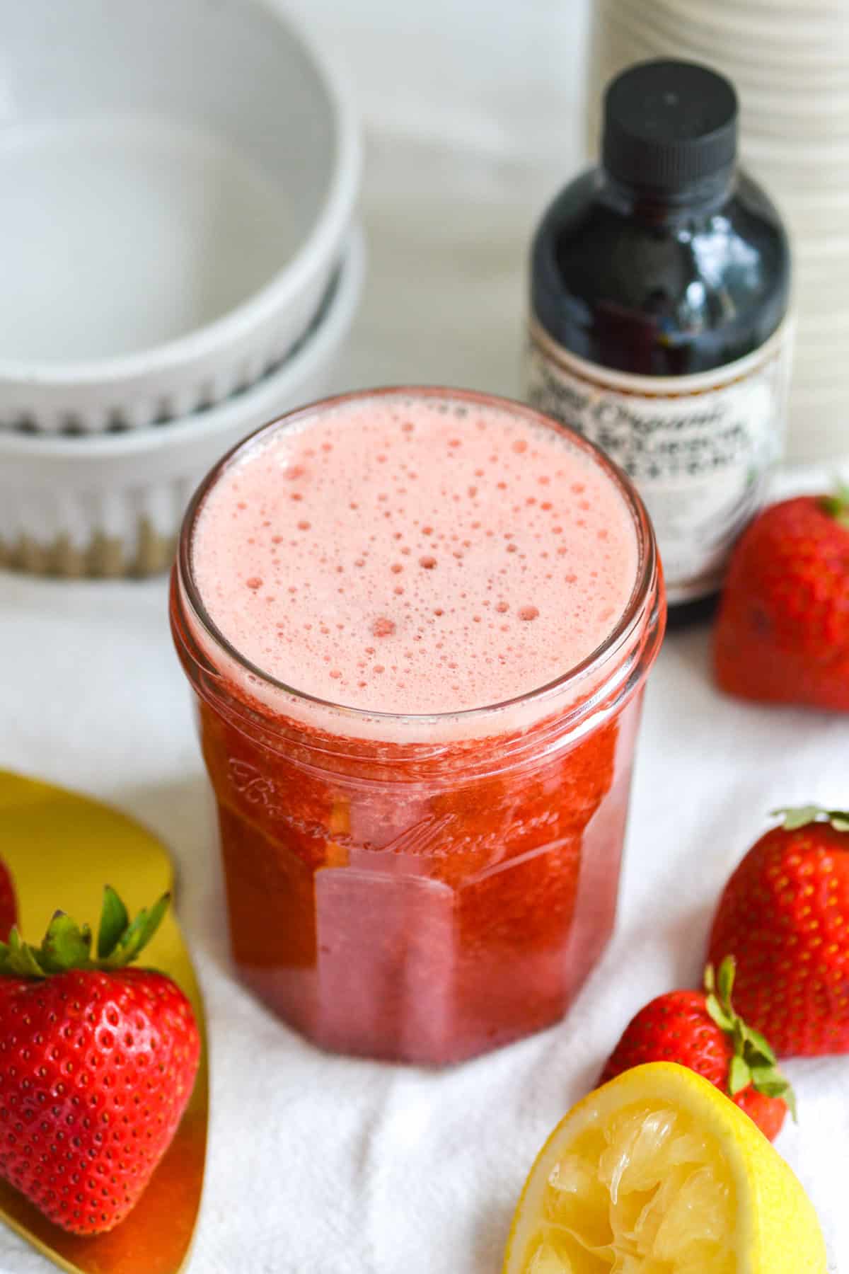 Strawberry syrup in a jar on a white cloth with strawberries in the foreground.