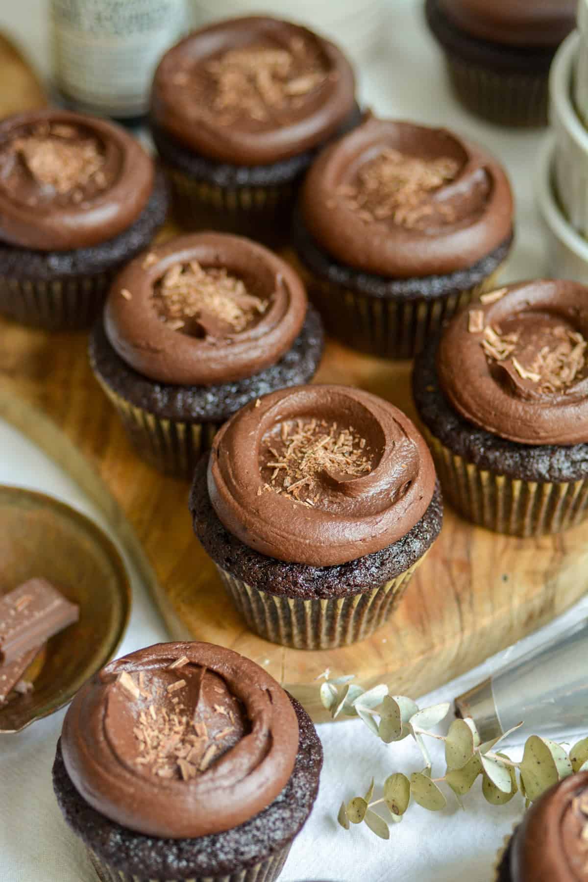 Vegan Chocolate Cupcakes topped with chocolate frosting on a small wooden cutting board.