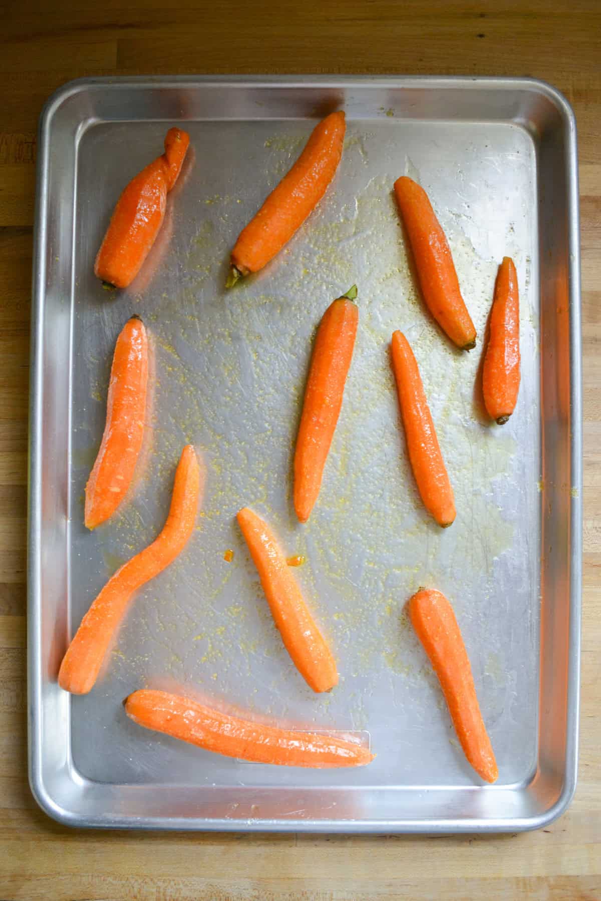 Peeled carrots coated in olive oil and spices on a baking sheet.