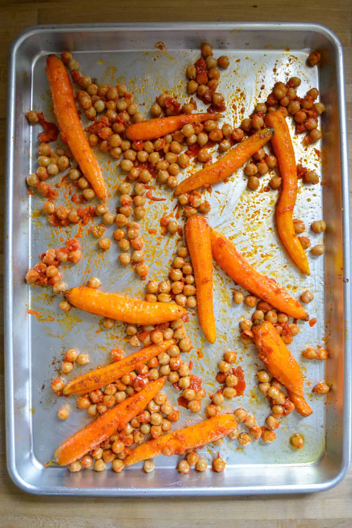 Roasted carrots and chickpeas coated with harissa on a baking sheet.