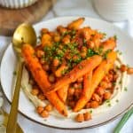 Harissa carrots and chickpeas garnished with chives on a plate with a gold fork next to it.