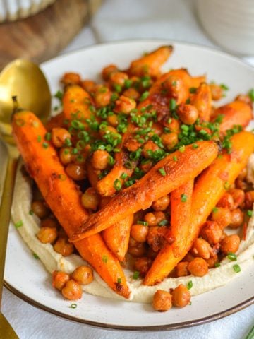 Harissa carrots and chickpeas garnished with chives on a plate with a gold fork next to it.