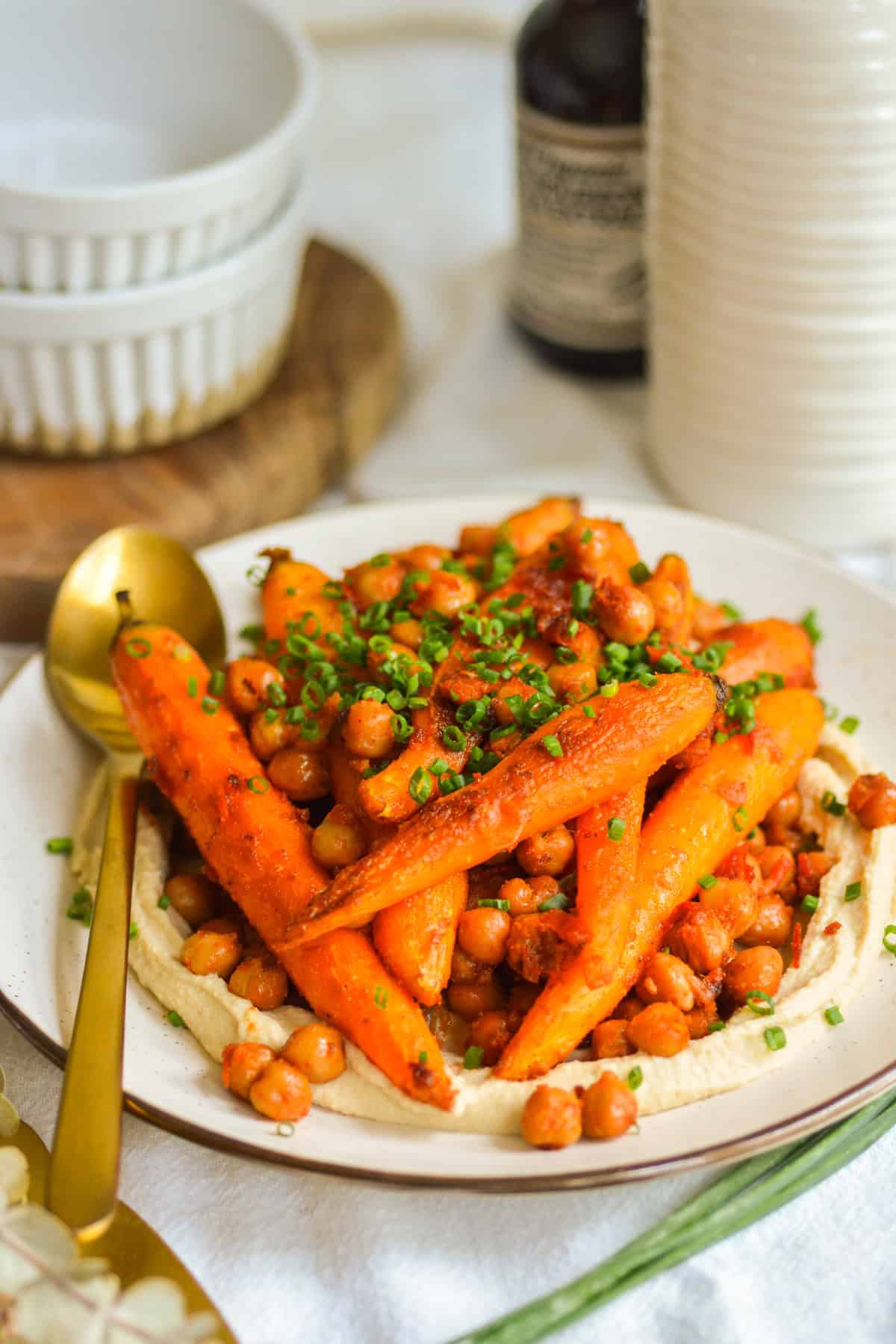 Roasted harissa carrots and chickpeas on top of hummus on a plate with a gold spoon.