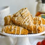 Vegan Pumpkin Scones with maple glaze on a white cake stand.
