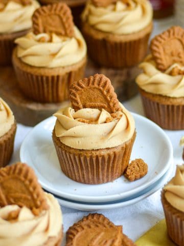 Biscoff Cupcake topped with a Biscoff cookie on a small plate with more cupcakes around the scene.