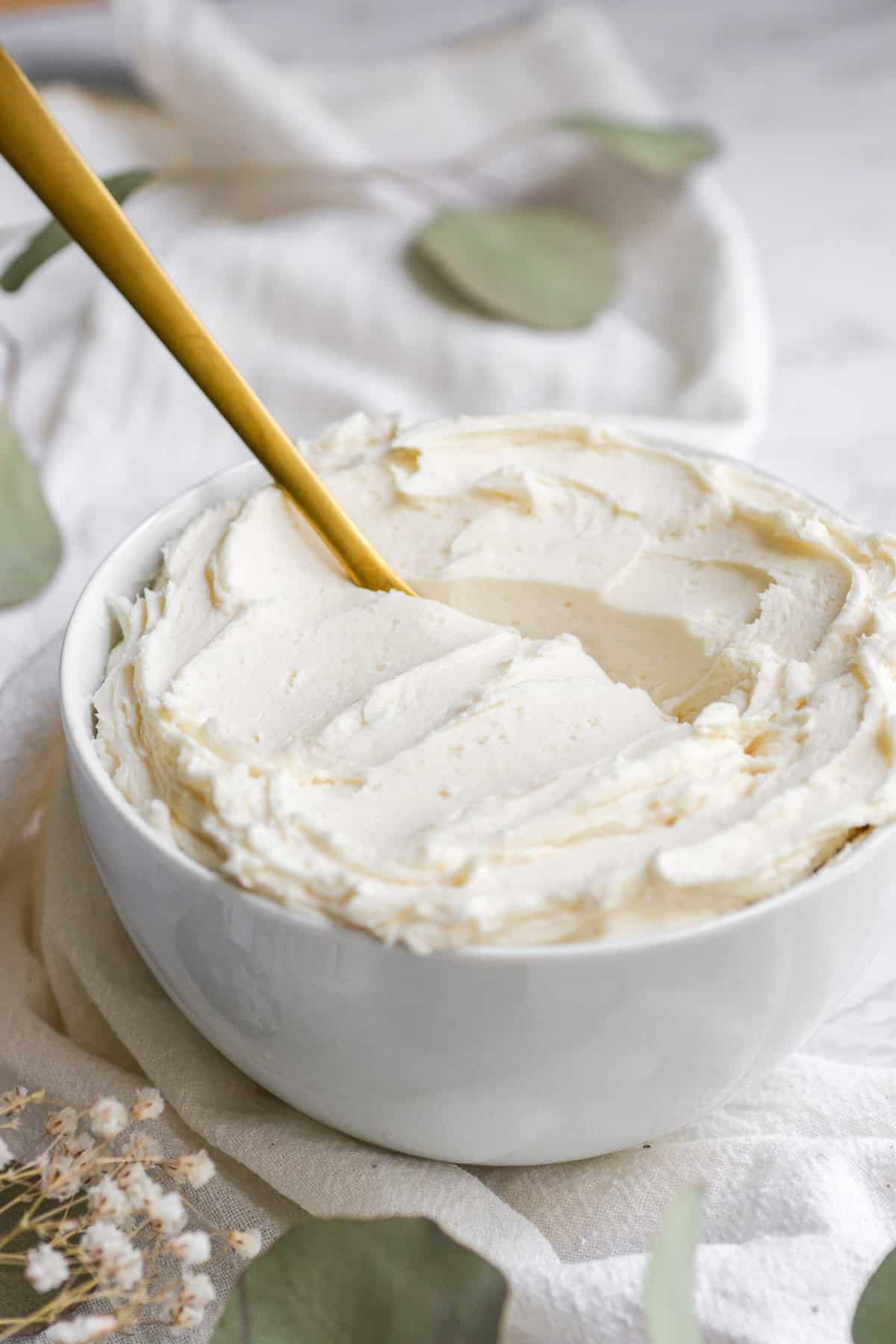 Vegan vanilla frosting in a bowl with a gold spoon in it.