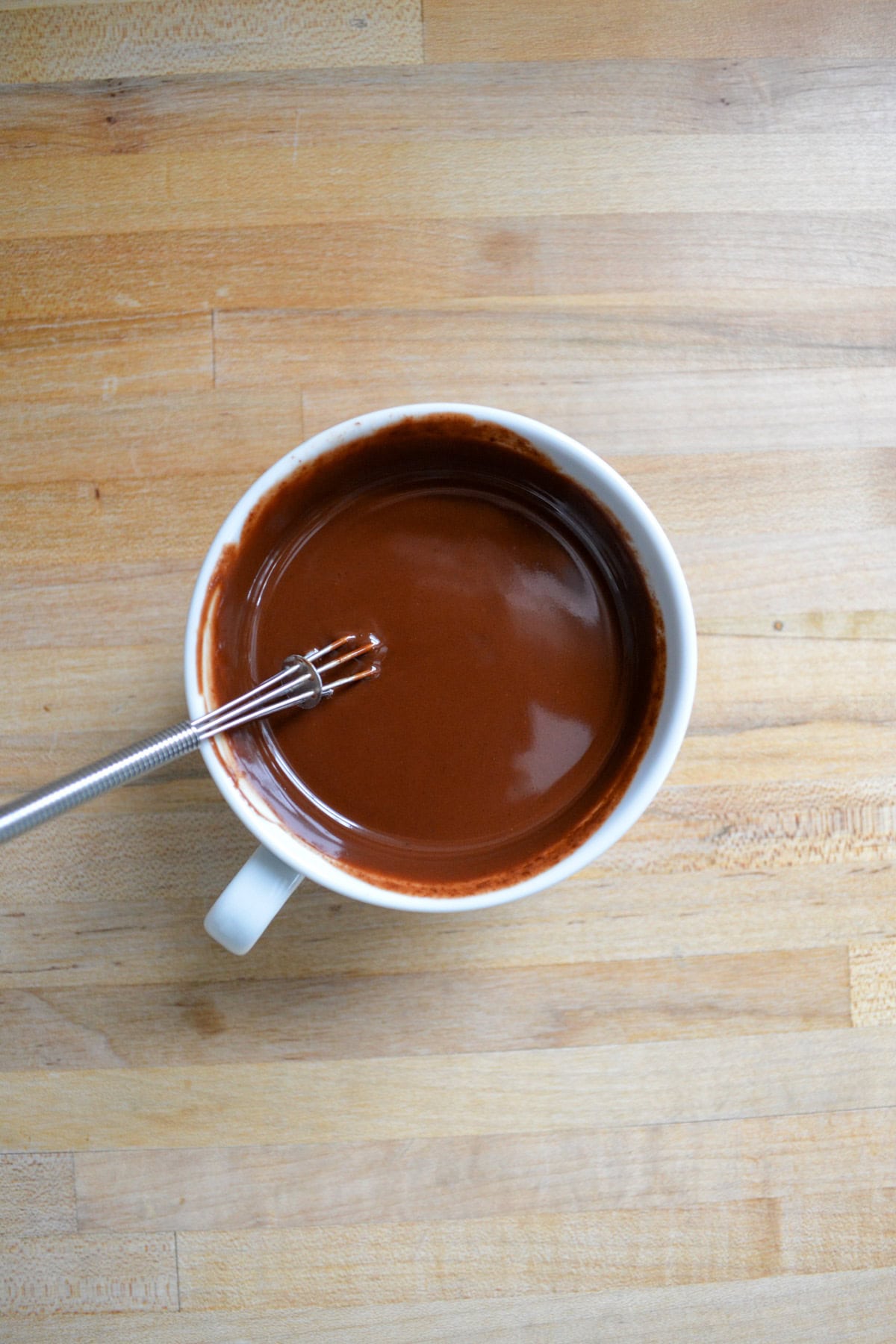 Vegan ganache in a small cup with a small whisk inside.