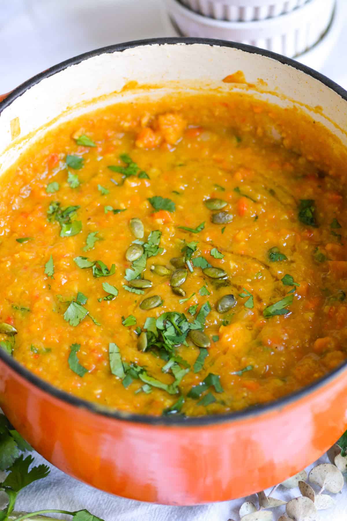 Carrot Red Lentil Soup in a Dutch-oven topped with roasted pumpkin seeds and chopped cilantro.